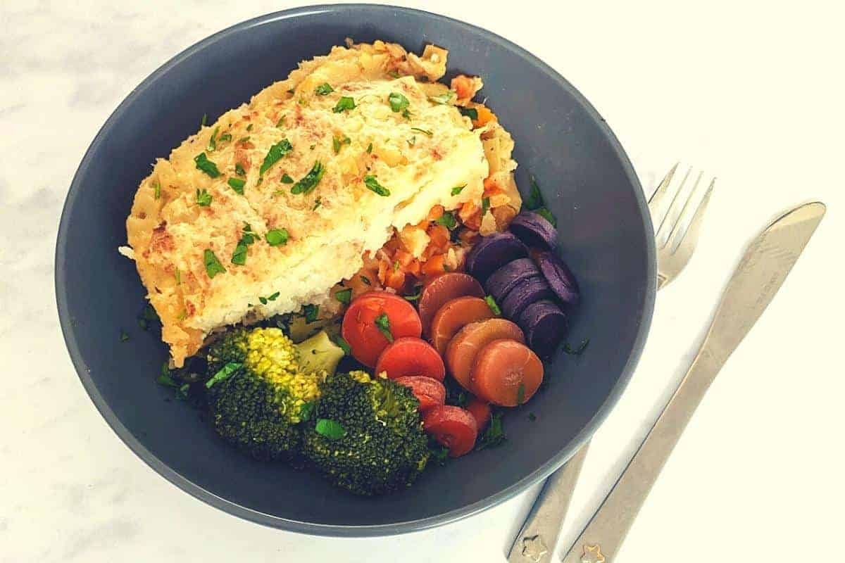 Gardeners pie served with different varieties of carrots and broccoli in a grey bowl.