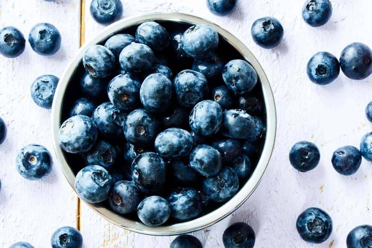 white bowl of blueberries with some spilt on a white table