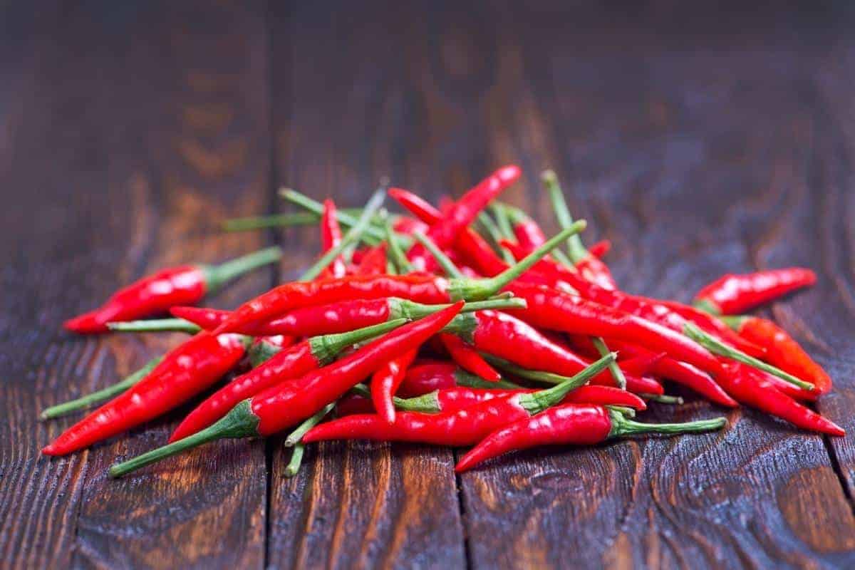 A pile of raw red chillies on a wooden board.