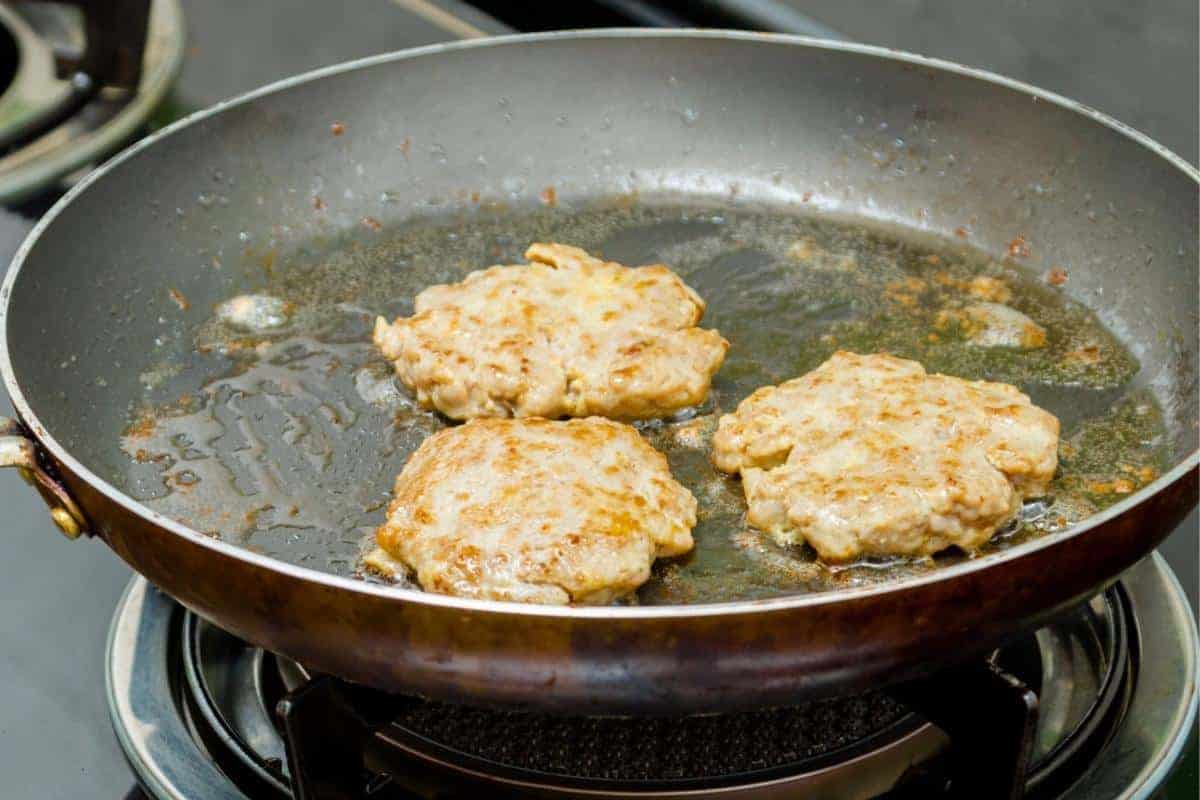 Pork burgers frying in a frying pan with oil.
