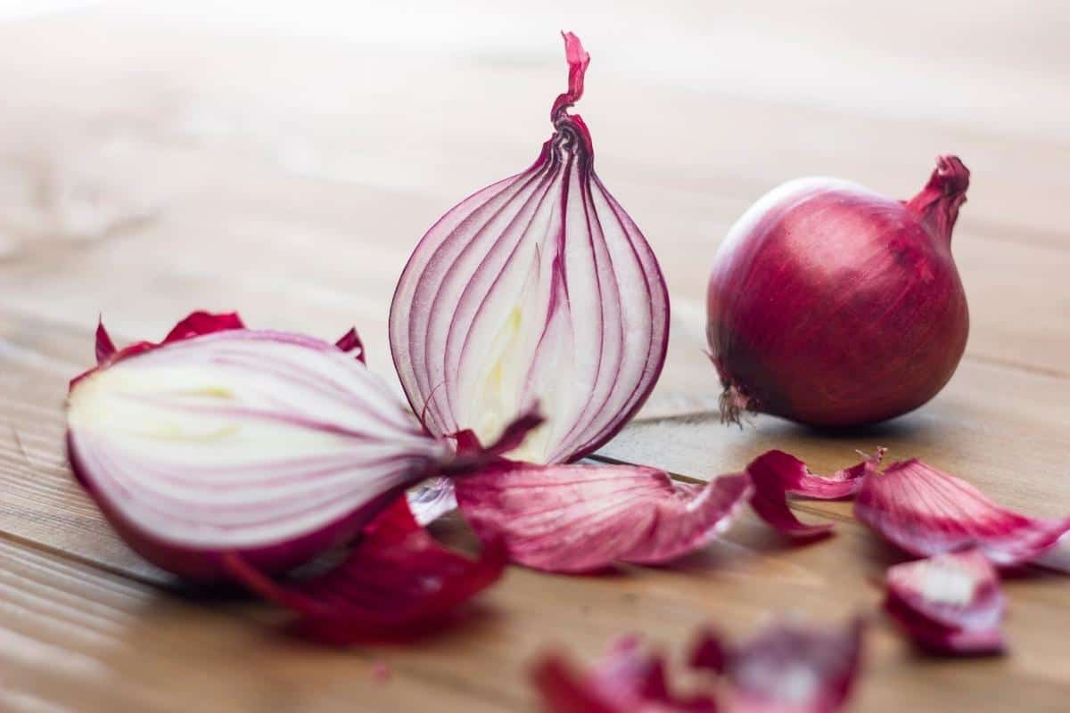 red onion whole with a halved red onion and some red onion pieces on a wooden table