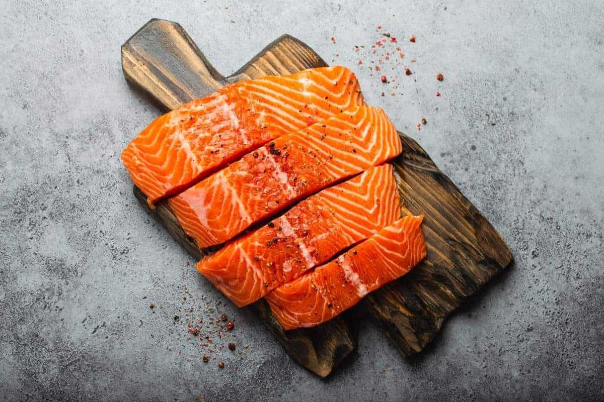 Wooden board with four salmon fillets.