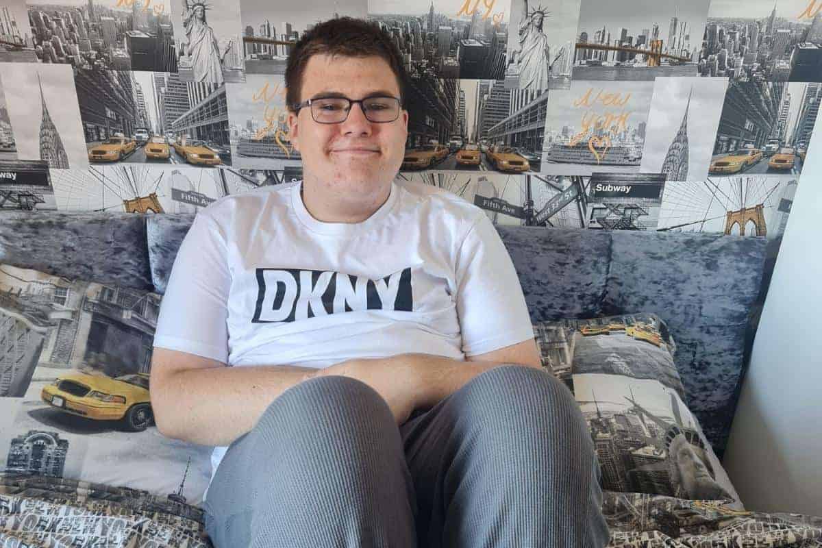 Teenage boy sitting on a bed in a grey New York themed bedroom wiht wallpaper and duvet cover both of the theme, he is smiling and wearing comfortable DKNY loungewear.