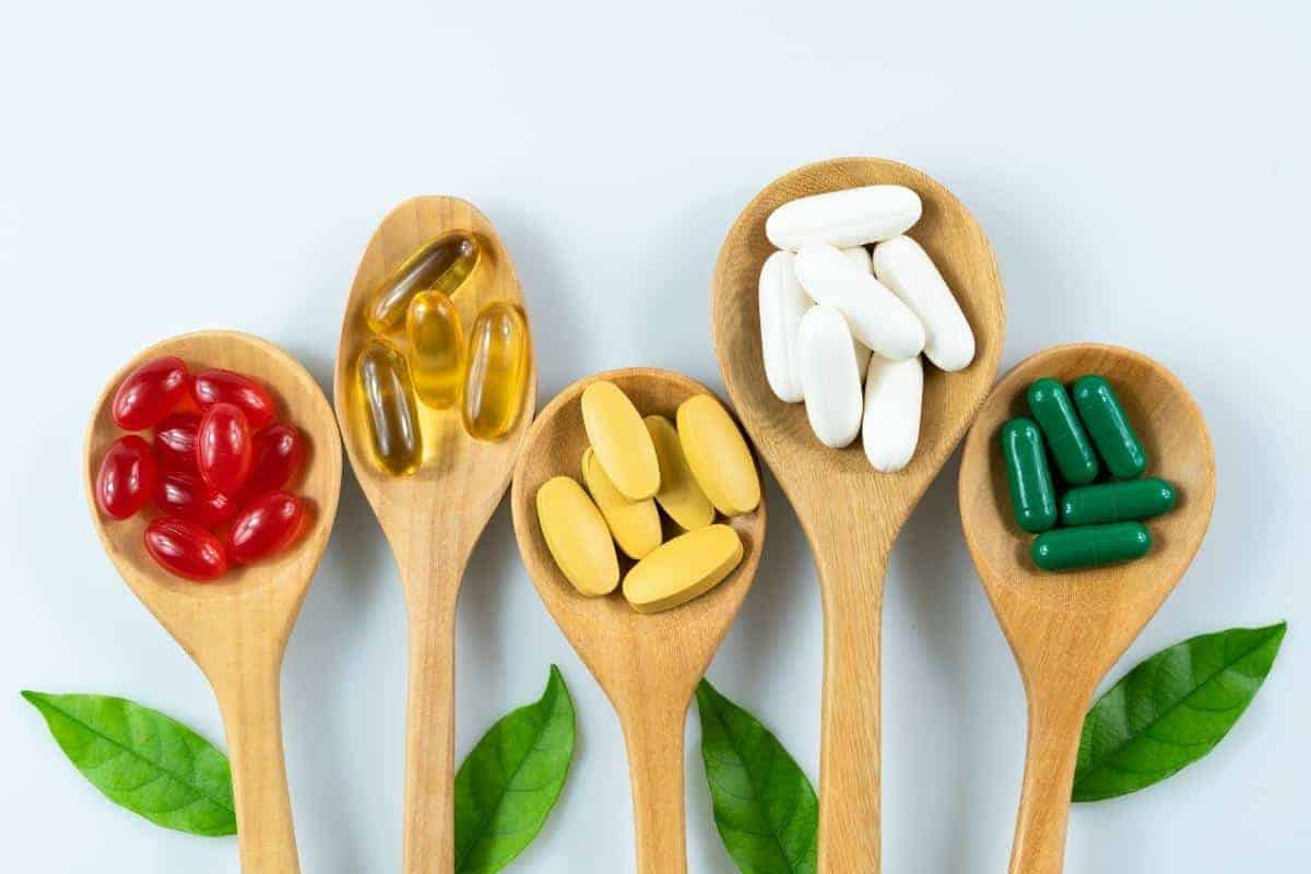 vitamins on wooden spoons on a plain background with capsules and tablets.