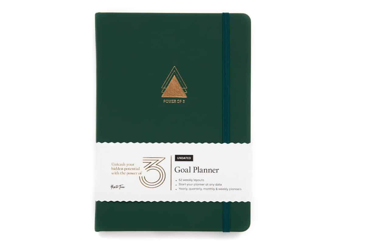 A green goal planner notebook with a gold triangle design on the cover, wrapped in a printed band featuring product information—a perfect gift idea for her and this would be a great suitable for Slimming World meal planner too!