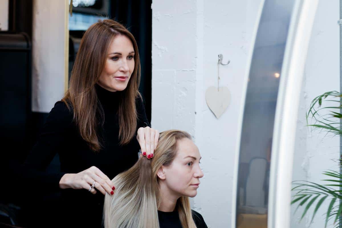 A hairdresser holding up hair extensions next to a blonde ladies hair.