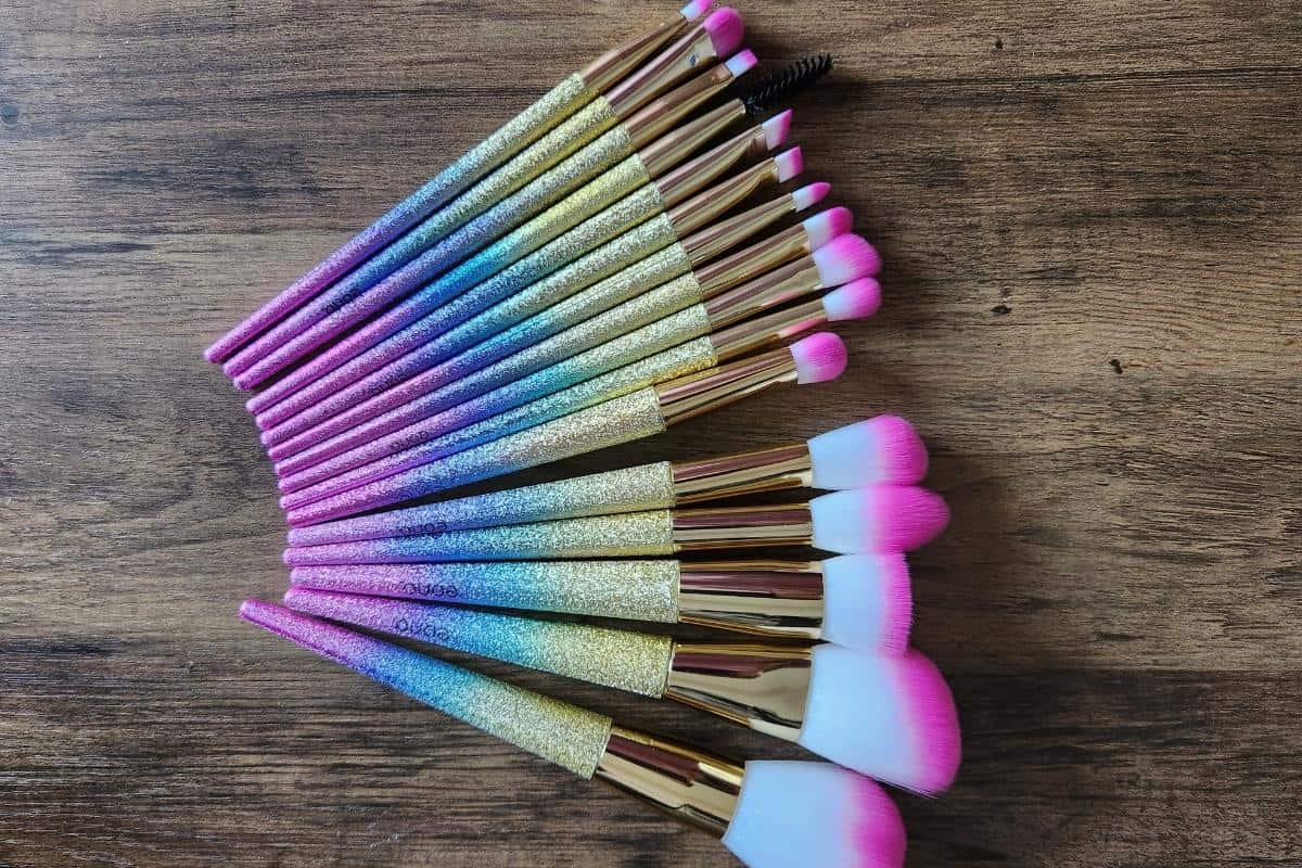 A bargain make-up set features dazzling makeup brushes with glittery handles in a gradient of pink, purple, and blue, beautifully arranged on a wooden surface.