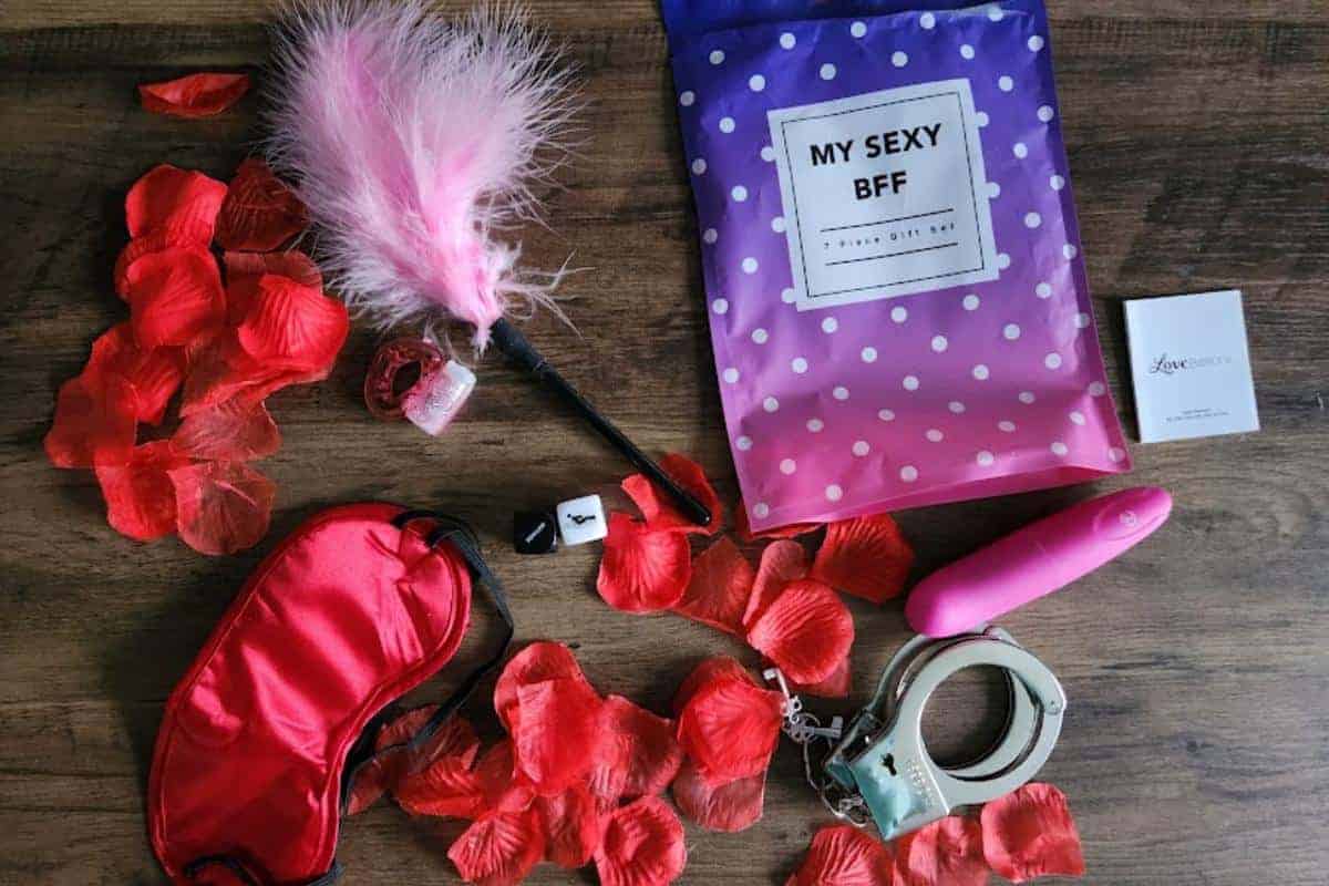 A selection of adult toys includiing blindfold, tickle stick, handcuffs and dice with artificial red rose petals.