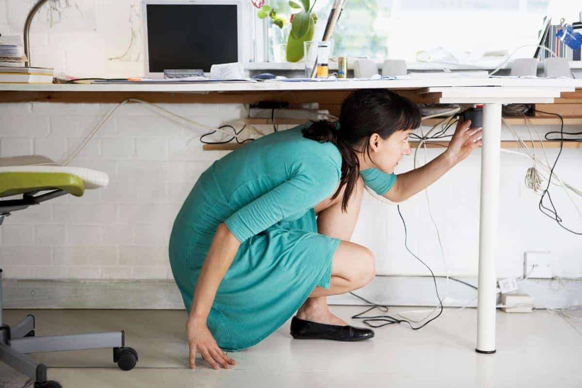 Lady crouching under a desk plugging in a plug and sorting out the wires.