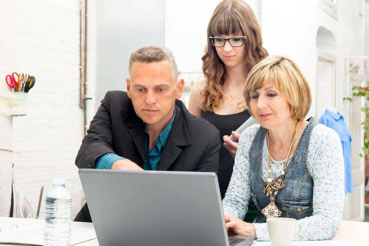 Parents and teenage girl all around a laptop on a desk.