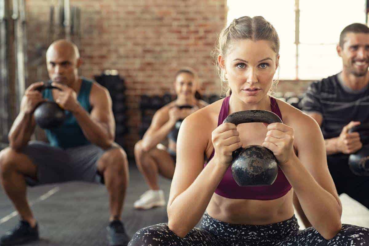 A kettlebell exercise class with a woman concentrating squatting holding a kettlebell in front of her chest.