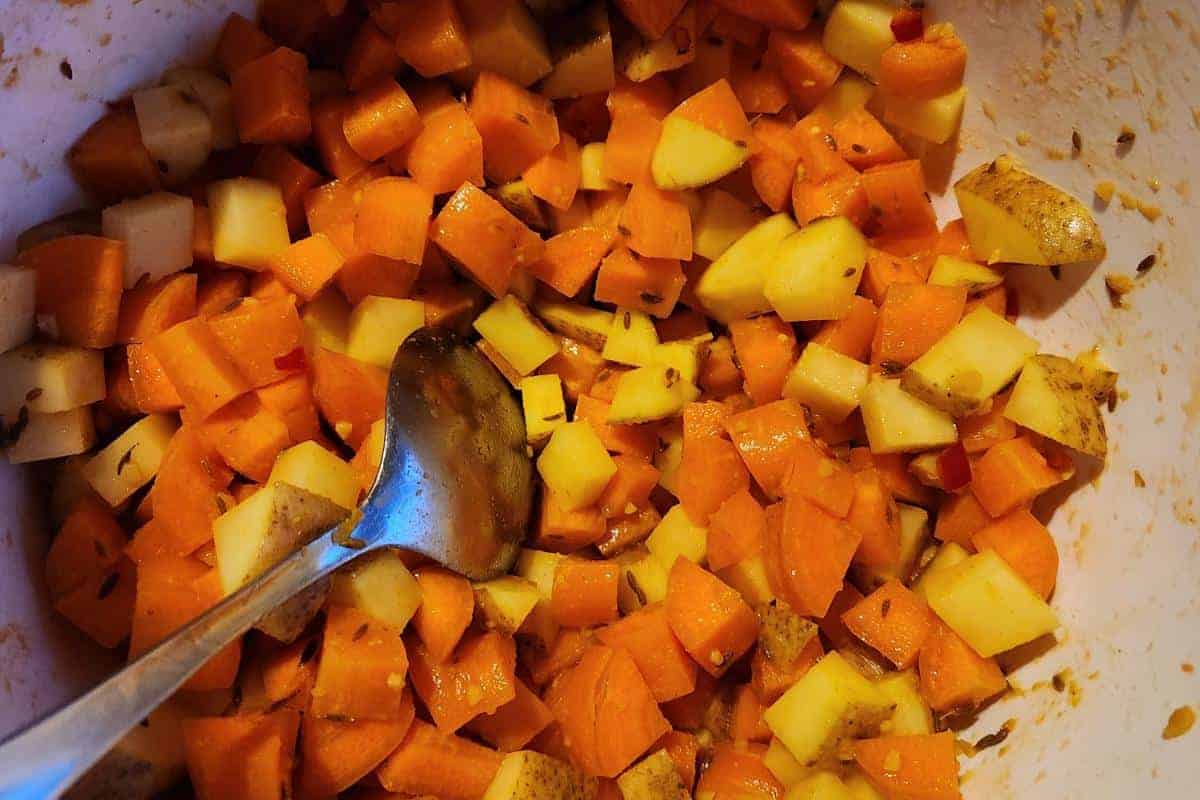diced potatoes, carrots and spices being mixed in a white bowl