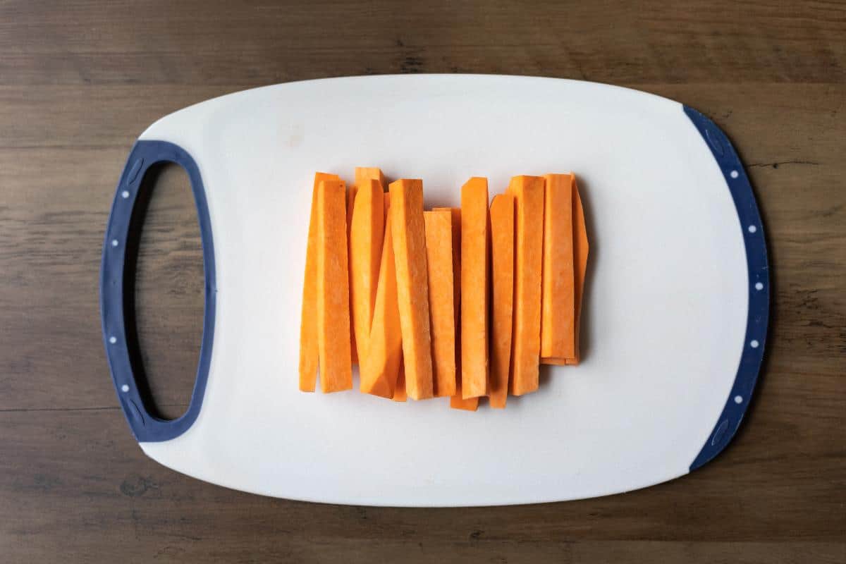 A chopping board with strips of raw sweet potato.