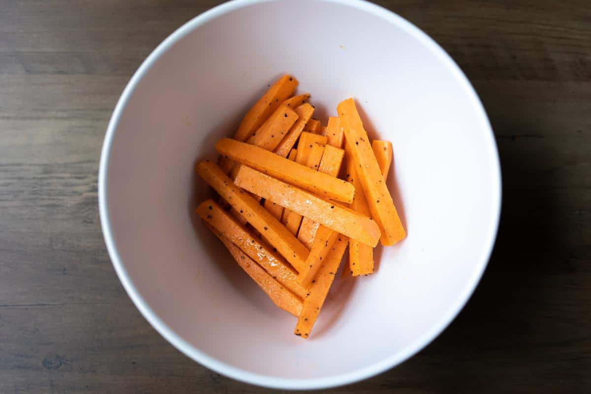 Raw sweet potato fries seasoned in a white bowl.