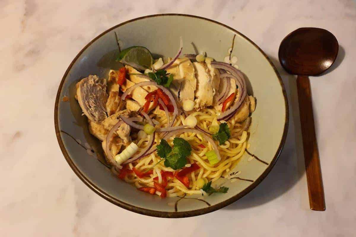 Bowl of chilli chicken ramen with chicken, red onion, spring onions and lime.