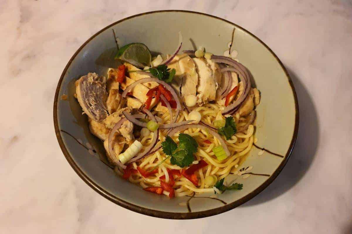 Bowl of chilli chicken ramen with chicken, red onion, spring onions and lime.