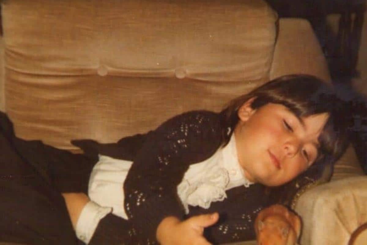 A young brunette girl laying on a tan leather sofa