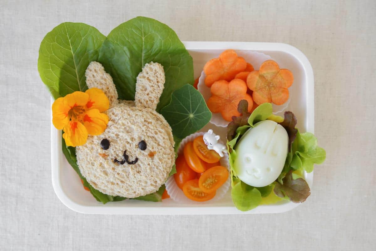 A cute lunchbox selection for kids with a bunny shaped sandwich and flower shaped carrot slices.