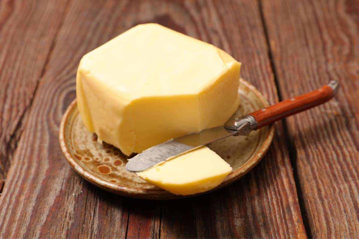 small brown plate on a wooden table with block of butter with corner cut off with a butter knife