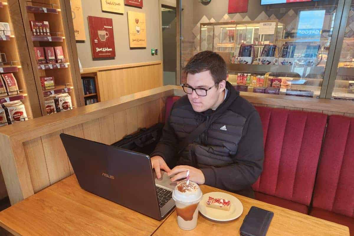 young man working on a laptop inside costa wearing an adidas jacket.