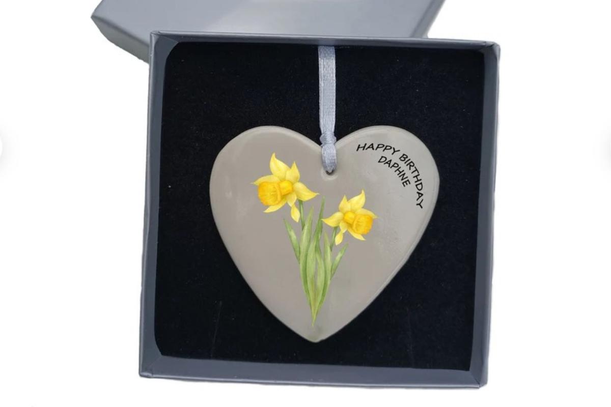 A hanging heart with a birth flower on in a velvet style case.