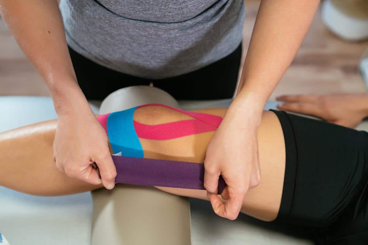 Hands putting kinesiology tape onto a ladies knee.