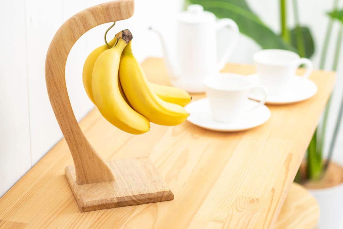 Bananas hanging on a wooden banana holder to keep them away from other fruit