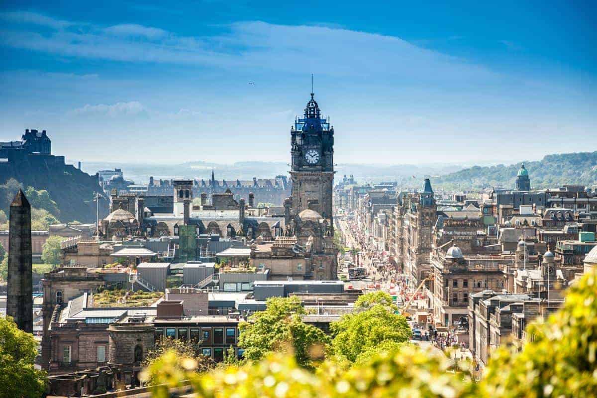 An aerial view of the city of Edinburgh with a bright blue sky and lots of old buildings.