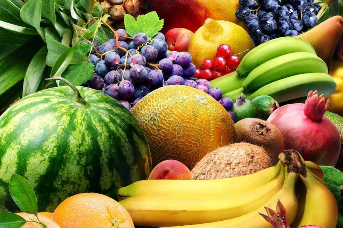 Pile of fresh fruit with grapes, melon, watermelon, bananas, lemon kiwi and plums.