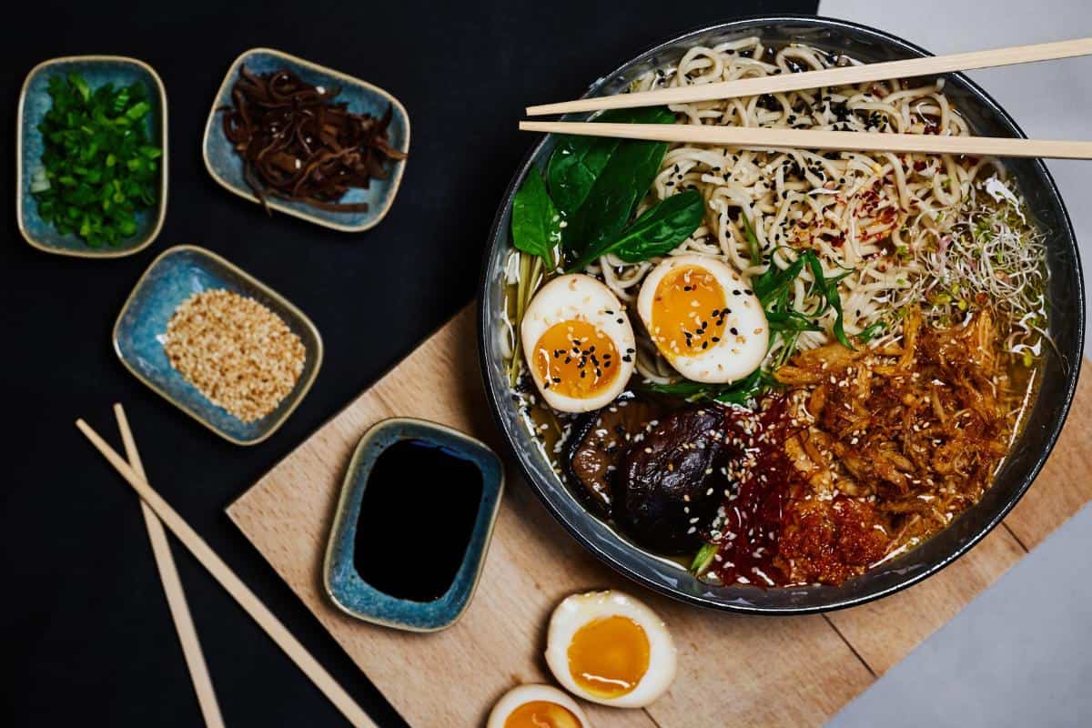 ramen noodles in a restaurant with soft boiled eggs slices in half, dipping sauces and chop sticks.