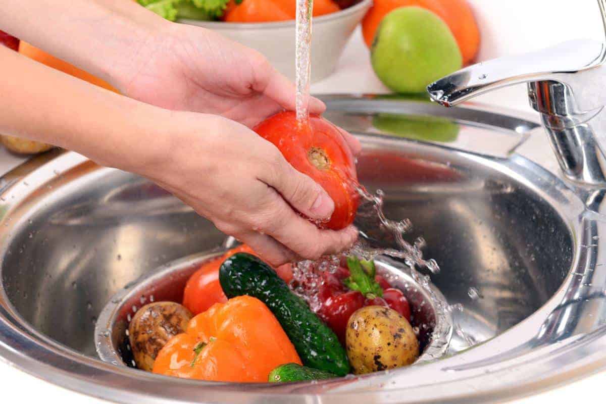 Ladies hands washing a selection of fruit and vegetables under the tap.