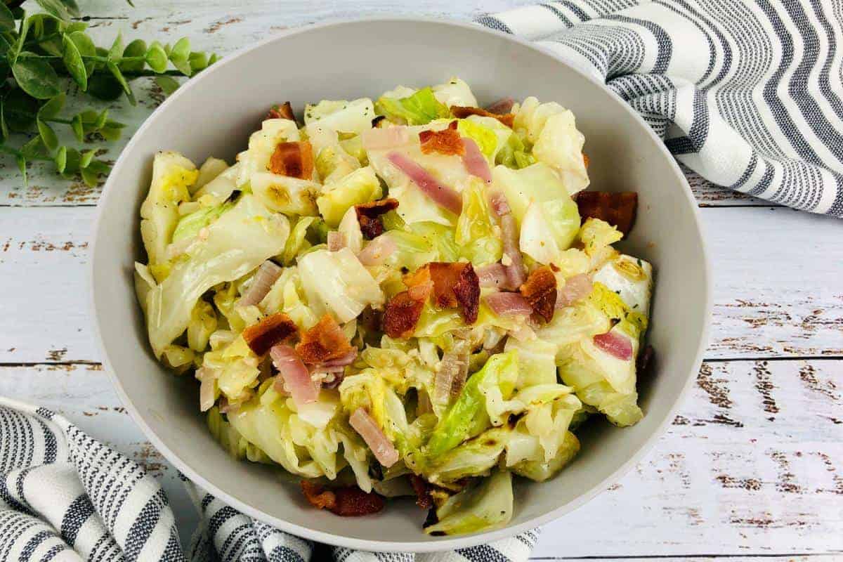 Bowl of fried cabbage with pieces of fried bacon and fried onion mixed in.