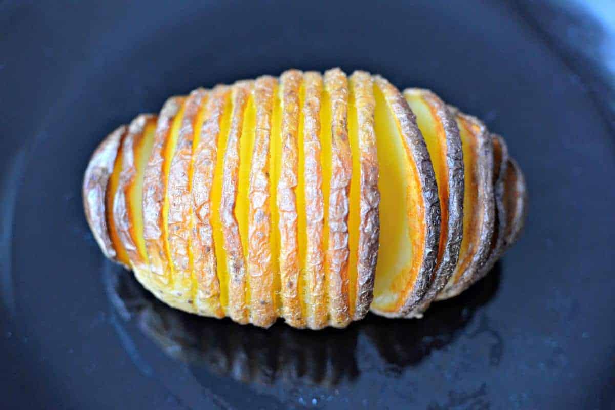a close up of a hasselback potato with a dark cooked outside and yellow fluffy potato inside.
