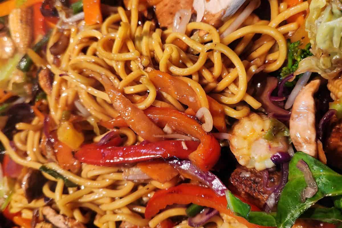 Singapore chow mein close up showing the sauce covering the noodles and colourful vegetables.