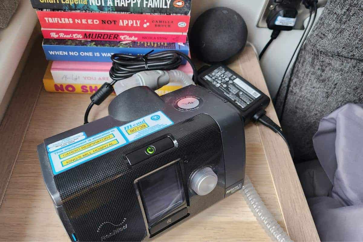 CPAP machine on a bedside table besides books.