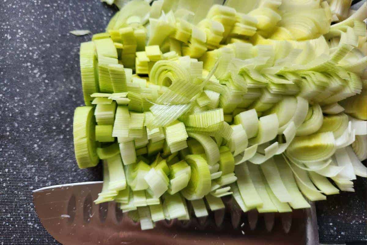 Sliced raw leeks on a chopping board with a knife.