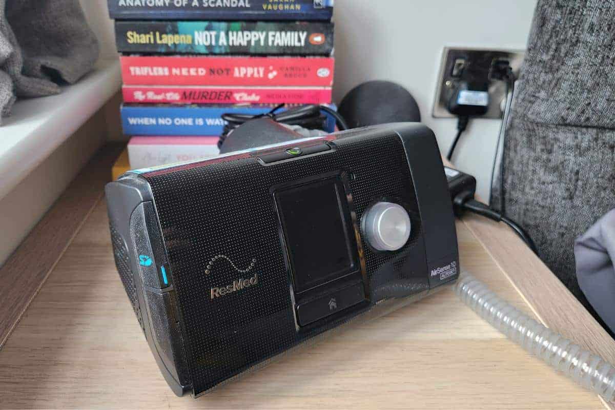 CPAP machine for sleep apnea on a bedside table besides books.
