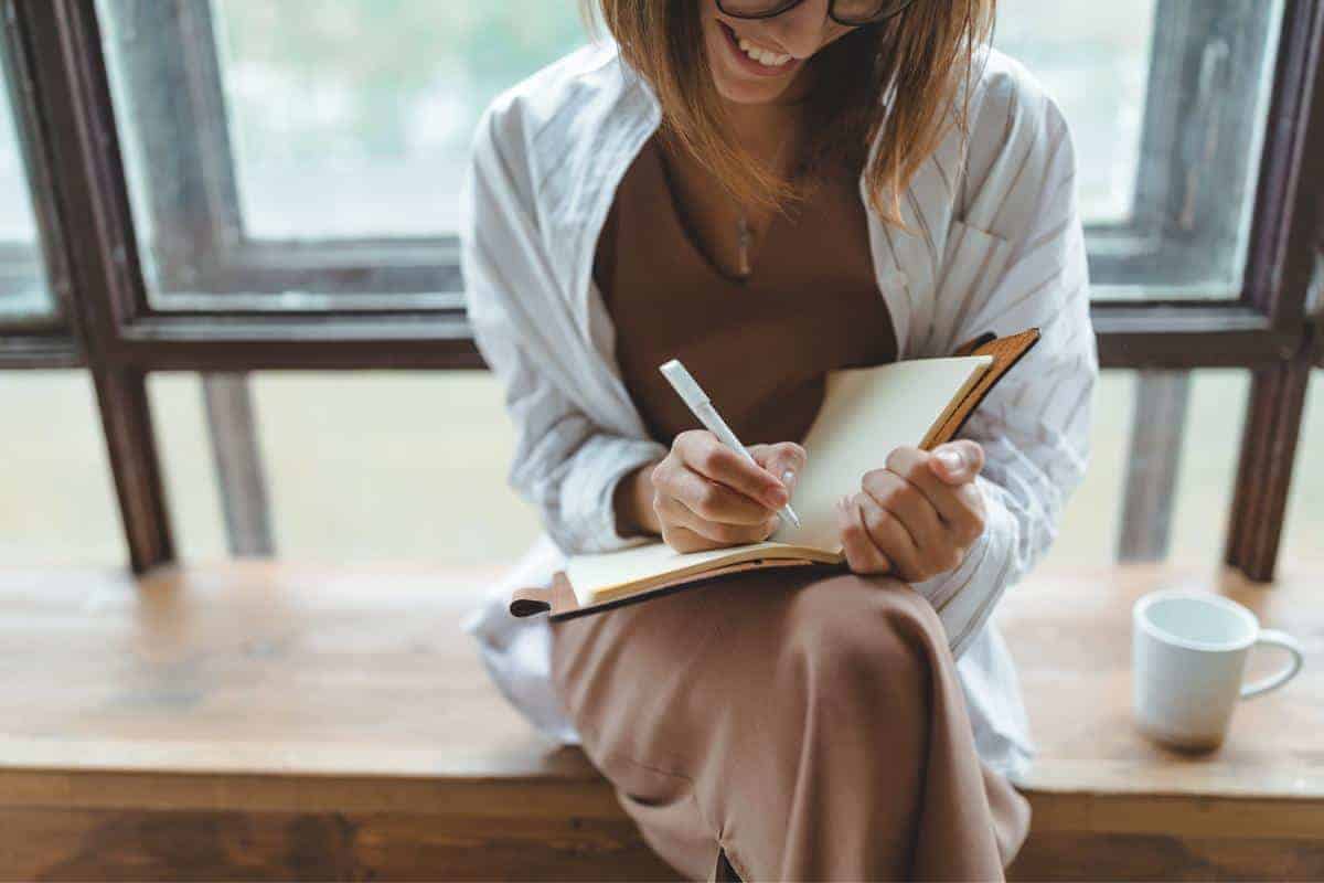 Smiling lady sitting with her legs crossed writing in a notebook.