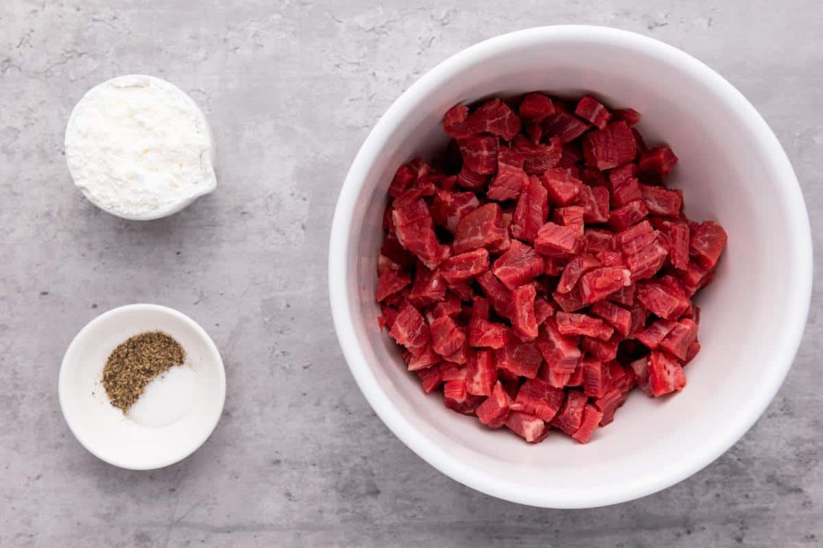 bowl of chopped flank steak with a small dish of cornstarch and another of salt and pepper.