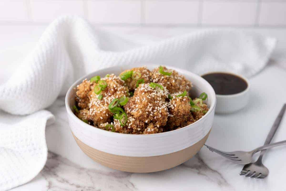 Bowl of teriyaki cauliflower wings topped with sesame seeds.