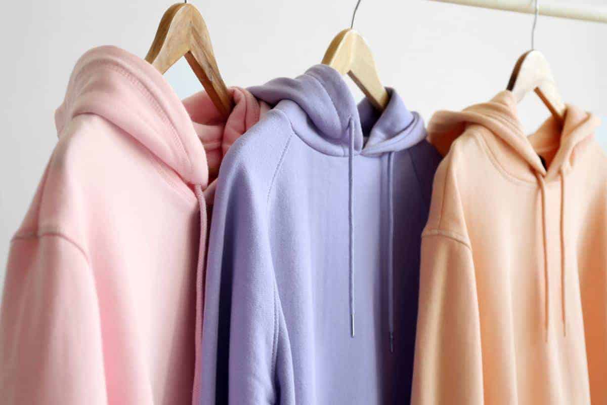 Three pastel coloured hoodies hanging on wooden coat hangers.
