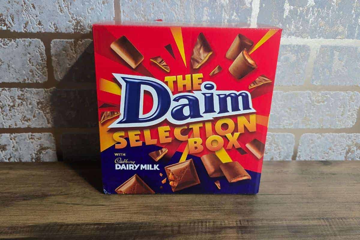 A red box labeled "The Daim Selection Box" makes the perfect gift, featuring assorted Daim chocolates and Cadbury Dairy Milk, set against a brick-patterned wall.