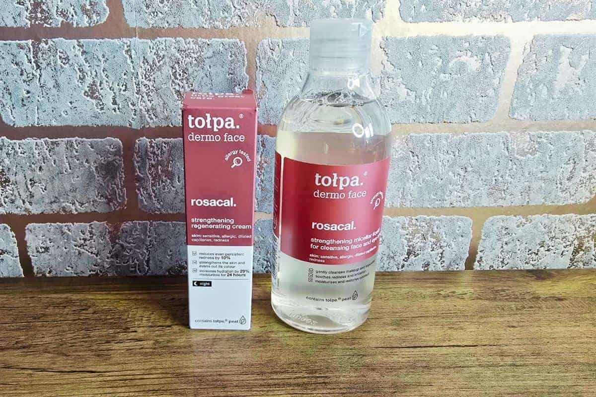 A box and bottle of Tołpa Dermo Face Rosacal products are elegantly placed on a wooden surface against a brick wall background, perfect for any Valentine's Day gift guide.