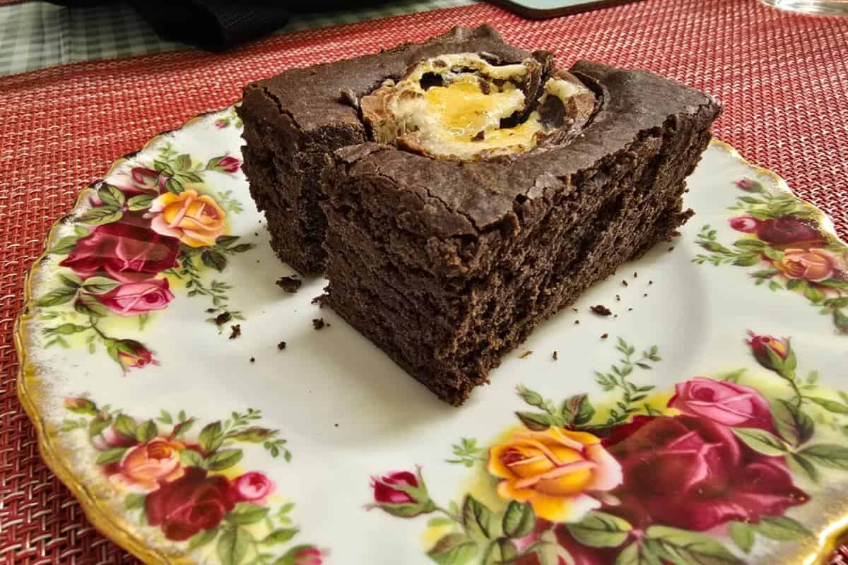A slice of chocolate cake on a floral-patterned plate rests elegantly on a red woven placemat, reminiscent of the delightful offerings at PoFfles Coffee and Cake Emporium in Mansfield.