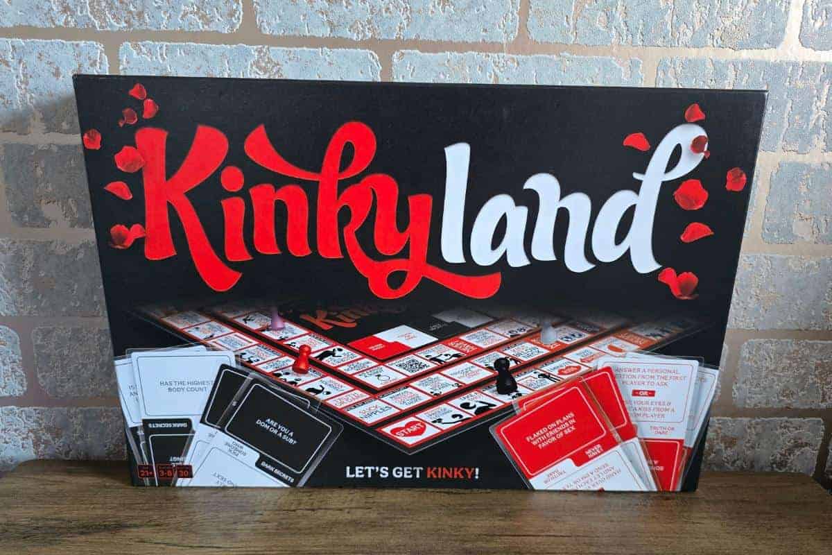 A board game box titled "Kinkyland" sits on a table, featuring a game board and cards. With the tagline "Let's get kinky!" against a rustic brick wall, this makes for a lovely gift that promises fun and excitement.