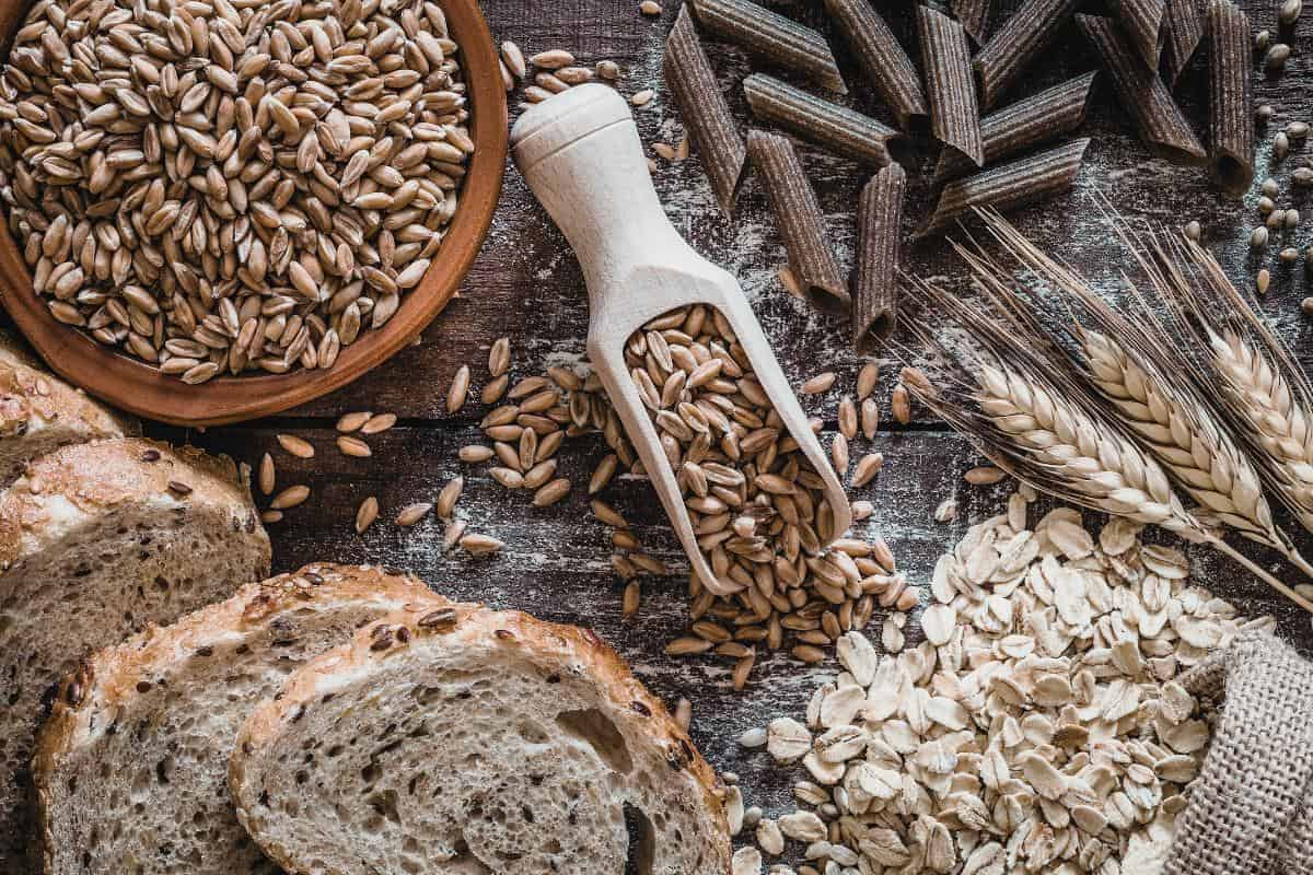 Various wholegrains and seeds, renowned for their nutrition and health benefits, are spread across a wooden surface, surrounded by slices of wholesome wholegrain bread and pasta.