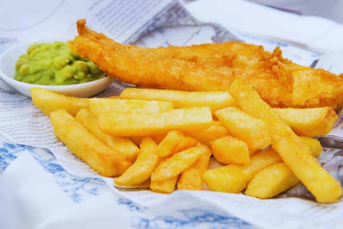 Deep-fried fish and chips served with mushy peas on newspaper print paper, blending traditional flavours with crispy perfection.