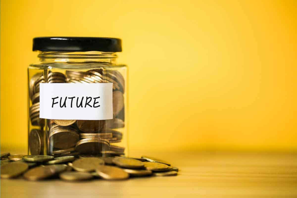 A glass jar labeled "FUTURE" brims with coins, echoing the promise of a Free Child Trust Fund. Scattered coins rest on a wooden surface, set against a vibrant yellow background.
