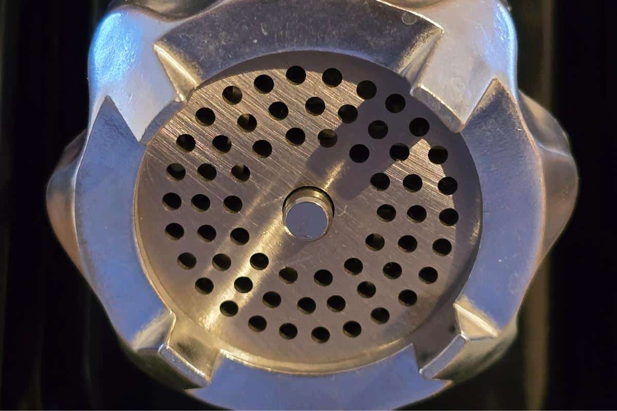 Close-up of a perforated silver metal surface with numerous small circular holes, reminiscent of an industrial component from an AAOBOSI electric meat grinder.