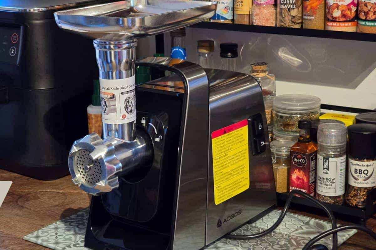 The AAOBOSI Electric Meat Grinder, with its robust 3000W power, sits elegantly on the kitchen counter, framed by an array of spices on the shelf behind it.